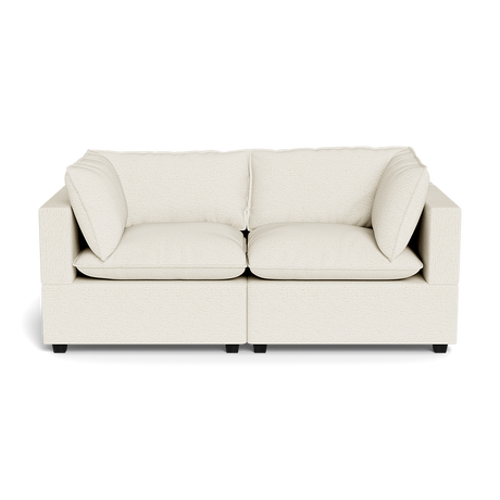The Kova Pillow Cushion Sofa 86" is a modern, cream-colored two-seater with squared arms and two large matching cushions, shown against a black background.