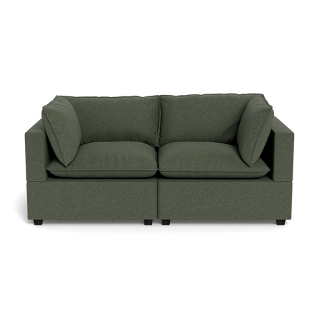 The Kova Pillow Cushion Sofa 86" is a modern dark green fabric sofa with thick seat and back cushions, two large side pillows, and square armrests, shown from the front against a black background.