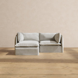 The Modular Performance 2-Seater Sectional, with its minimalist light gray cushions, sits on a wooden floor against a beige wall, creating a simple and cozy ambiance.