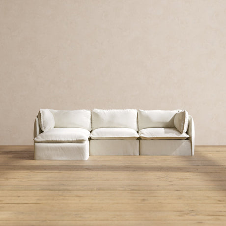 In a minimalist room, a Modular Performance 3-Seater Sectional is positioned against a beige wall on a wooden floor. The sectional boasts plush cushions and an inviting appearance.