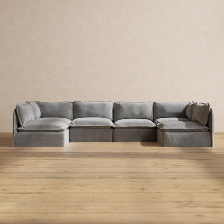 A Modular Performance 6-Seater Open-Ends U-Sectional in Plush Weave Ash is arranged against a plain beige wall, while the wooden floor beneath provides a warm contrast to the sofa's neutral tones.