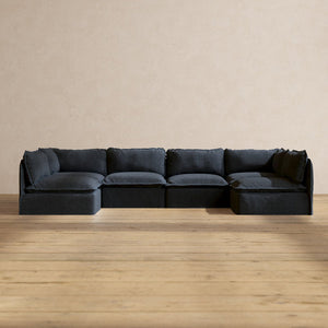 The Modular Performance 6-Seater Open-Ends U-Sectional in Plush Weave Ash is positioned against a beige wall and rests on a light wood floor. Its minimalist design fosters a modern and cozy atmosphere.