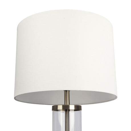 The Luna Table Lamp features a transparent cylindrical base with a metallic rim, white cylindrical lampshade, and an on/off switch, offering sleek and minimalist design perfect for contemporary interiors.