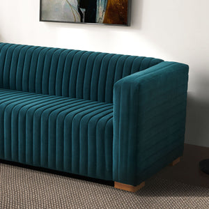 The Elara - Upholstered Sofa in teal velvet with vertical tufting and wooden feet sits on a textured gray carpet, with part of an abstract painting visible on the light-colored wall behind it.