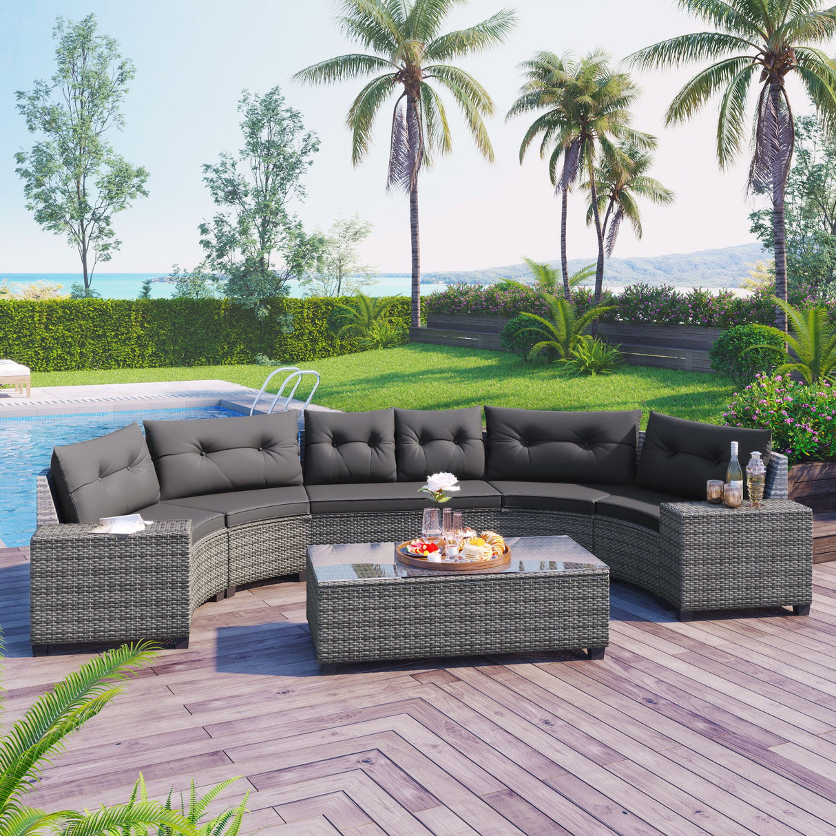The 8 Pieces Outdoor Wicker Round Sofa Set, featuring a curved design with dark cushions and a rectangular glass-top coffee table, graces a wooden deck next to a pool. The area is surrounded by palm trees, lush greenery, and offers a scenic ocean view.