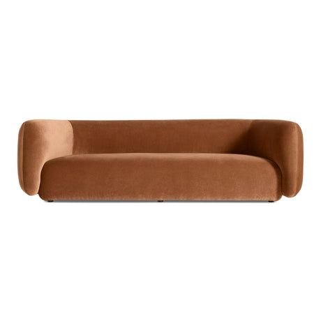 The Bustle Sofa in copper velvet features a modern, minimalist design with rounded arms and a low backrest, showcased against a plain white background.