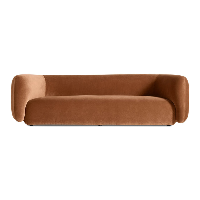 The Bustle Sofa in copper velvet features a modern, minimalist design with rounded arms and a low backrest, showcased against a plain white background.