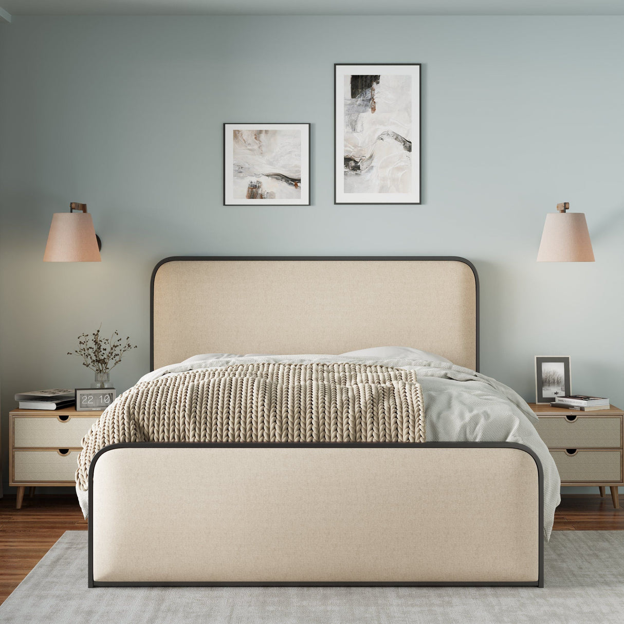 A minimalist bedroom features a light-colored Modern Bed with Curved Upholstered Headboard and Footboard and heavy-duty metal slats, flanked by wooden nightstands. Two abstract paintings hang above. Beige lamps and a woven blanket add warmth, with walls painted in soft mint green.