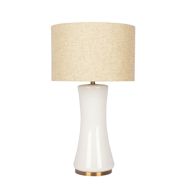 The Cascade lamp features a sleek white ceramic base with an hourglass shape, a beige fabric drum shade, and a brass-colored platform.
