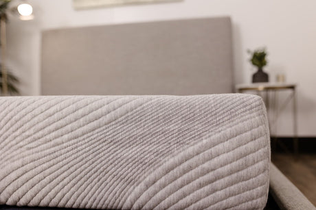 Close-up of the 8" Comfort Series Firm Gel Memory Foam Tight Top Mattress in light gray, featuring a textured, stitched surface, displayed with a matching upholstered headboard and a bedside table with a small plant.