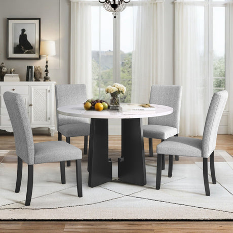 A dining room features a 5 Piece Round Dining Table Set, including a table and four gray upholstered chairs. The space is decorated with flowers and fruit on the table, complemented by a white rug, chandelier, cabinet, and window with sheer curtains.