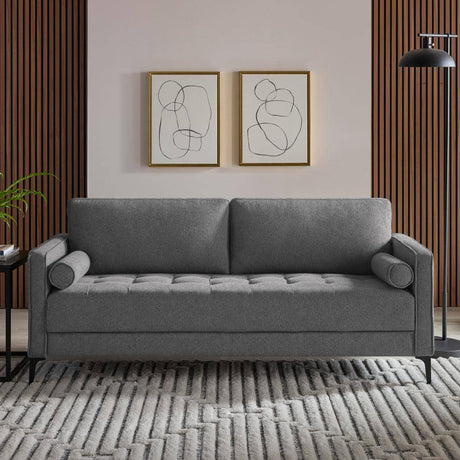 A modern living room featuring the StyleWell Goodwin Mid-Century Modern Sofa with throw pillows on a patterned rug. The wall behind showcases two abstract line drawings and is accented with vertical wooden panels. A tall black floor lamp and a small side table with a plant complete the scene.