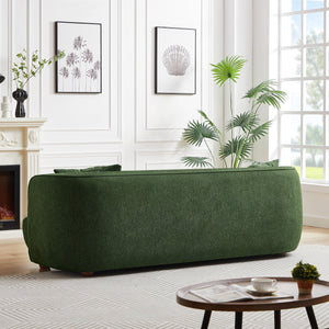 Facing large windows, a modern living room features a Larisa Mid-Century Modern Linen Sofa. Minimalist decor includes framed botanical prints, a potted plant, and a round wooden coffee table with a book and teacup, all harmonized by neutral walls and flooring.