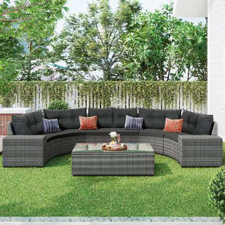 The outdoor patio features an 8-piece wicker round sofa set with a curved gray sectional and black cushions, adorned with orange-patterned pillows. A matching rectangular wicker coffee table holds a tray with books and a small plant, complementing the green lawn, white fence, and trees for added coziness.