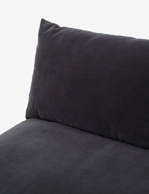 A close-up of the Decima Sectional Sofa showcases its black cushioned design with a plush pillow backrest. The soft and smooth fabric creates a cozy and inviting appearance. The simple light gray background highlights the dark color of the sofa.