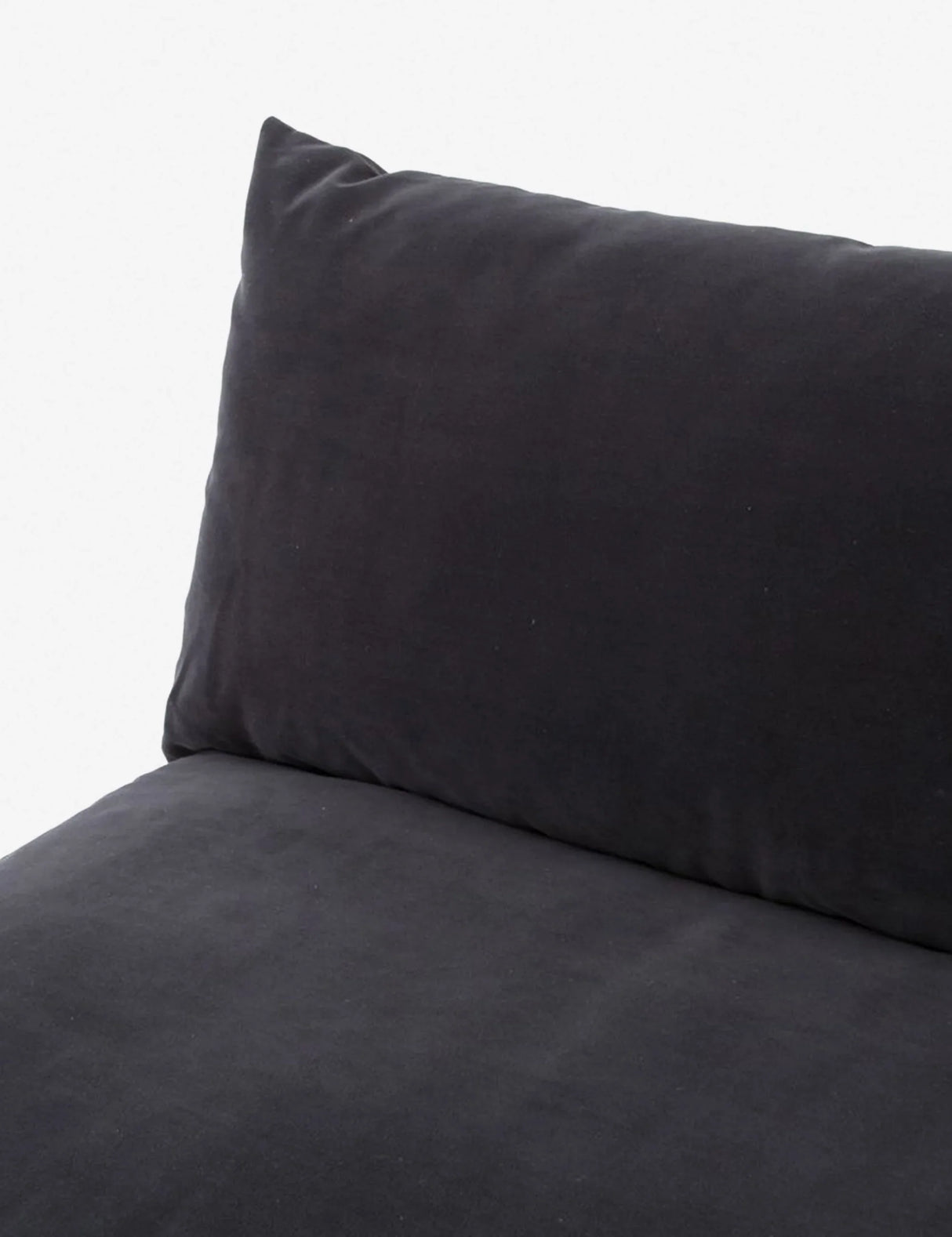 A close-up of the Decima Sectional Sofa showcases its black cushioned design with a plush pillow backrest. The soft and smooth fabric creates a cozy and inviting appearance. The simple light gray background highlights the dark color of the sofa.