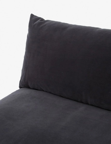 A close-up of the Decima Sectional Sofa showcases its black cushioned design with a plush pillow backrest. The soft and smooth fabric creates a cozy and inviting appearance. The simple light gray background highlights the dark color of the sofa.