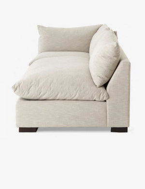 The Decima Sectional Sofa, featuring a beige color and an L-shaped design, is positioned against a white background. It boasts two large cushions, thick plush cushioning, and dark rectangular legs.