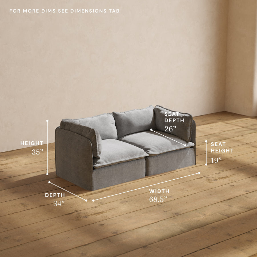 A Modular Performance 2-Seater with Sink-in Comfort Cushion, in gray, is positioned against a beige wall on a wooden floor. The dimensions are labeled as follows: Height 35", Depth 34", Width 68.5", Seat Depth 26", and Seat Height 19". For more detailed information, please refer to the dimensions tab.