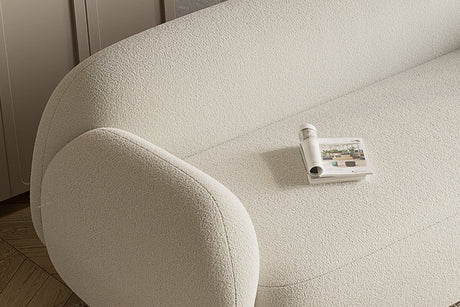 A close-up of the light beige textured Dori Sofa by Acanva, with a rolled-up magazine resting on one of its seats. The sofa is positioned on a wooden floor, beside a cabinet.