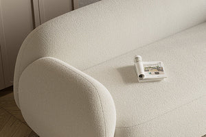 A close-up of the light beige textured Dori Sofa by Acanva, with a rolled-up magazine resting on one of its seats. The sofa is positioned on a wooden floor, beside a cabinet.