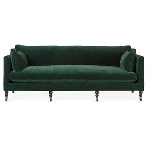 Introducing the Margot Velvet Sofa: a dark green masterpiece with round cushions at each end, supported by elegant wooden legs and featuring a classic design. It boasts a straight back and sleek armrests for added sophistication.