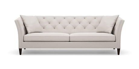 Introducing the Shelton 98" Sofa: a cream-colored masterpiece with a contemporary flair, featuring a tufted backrest and two perfectly matching throw pillows. The design boasts sleek, slightly flared arms complemented by elegant wooden legs, all showcased against a plain white backdrop.