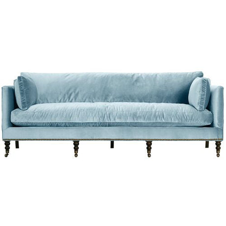 Introducing the Margot Velvet Sofa: a light blue sofa featuring a luxurious velvet fabric, complemented by a spacious long cushioned seat and cylindrical side cushions. It boasts a sleek straight backrest and stands gracefully on dark wooden legs with subtle casters for easy mobility.