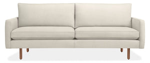 The 86" Jasper Sofa is a modern, minimalist piece featuring a beige color with a straight back and two seat cushions. It boasts sleek armrests and wooden legs, offering a contemporary look, all set against a plain white background.