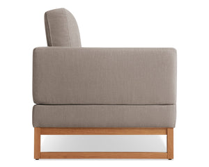 Side view of a modern gray upholstered armchair with a light wooden base. The chair has a rectangular shape and a minimalist design.