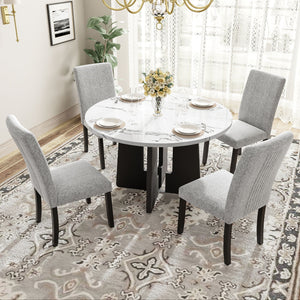 A stylish dining room showcases a 5 Piece Round Dining Table Set with four gray upholstered chairs. The white table is adorned with plates and a vase of yellow flowers, set atop a patterned rug. A luscious plant and lace-curtained window complete the elegant ambiance.