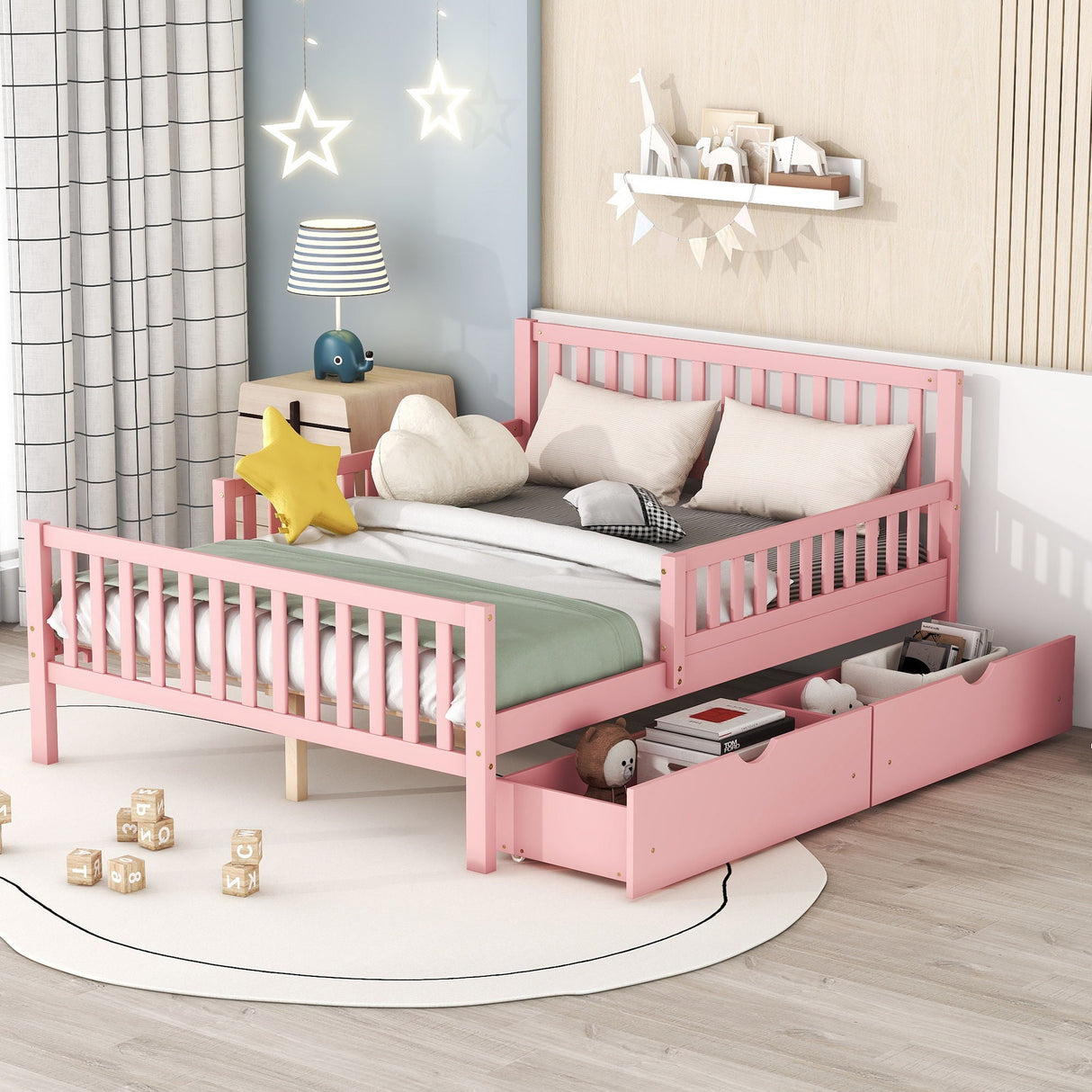 A children's bedroom includes a pink platform bed with guardrails and two storage drawers filled with toys, adorned with star and cloud cushions. The room features light wood flooring, a wall-mounted bookshelf, star-shaped lights, and a round rug scattered with wooden blocks.