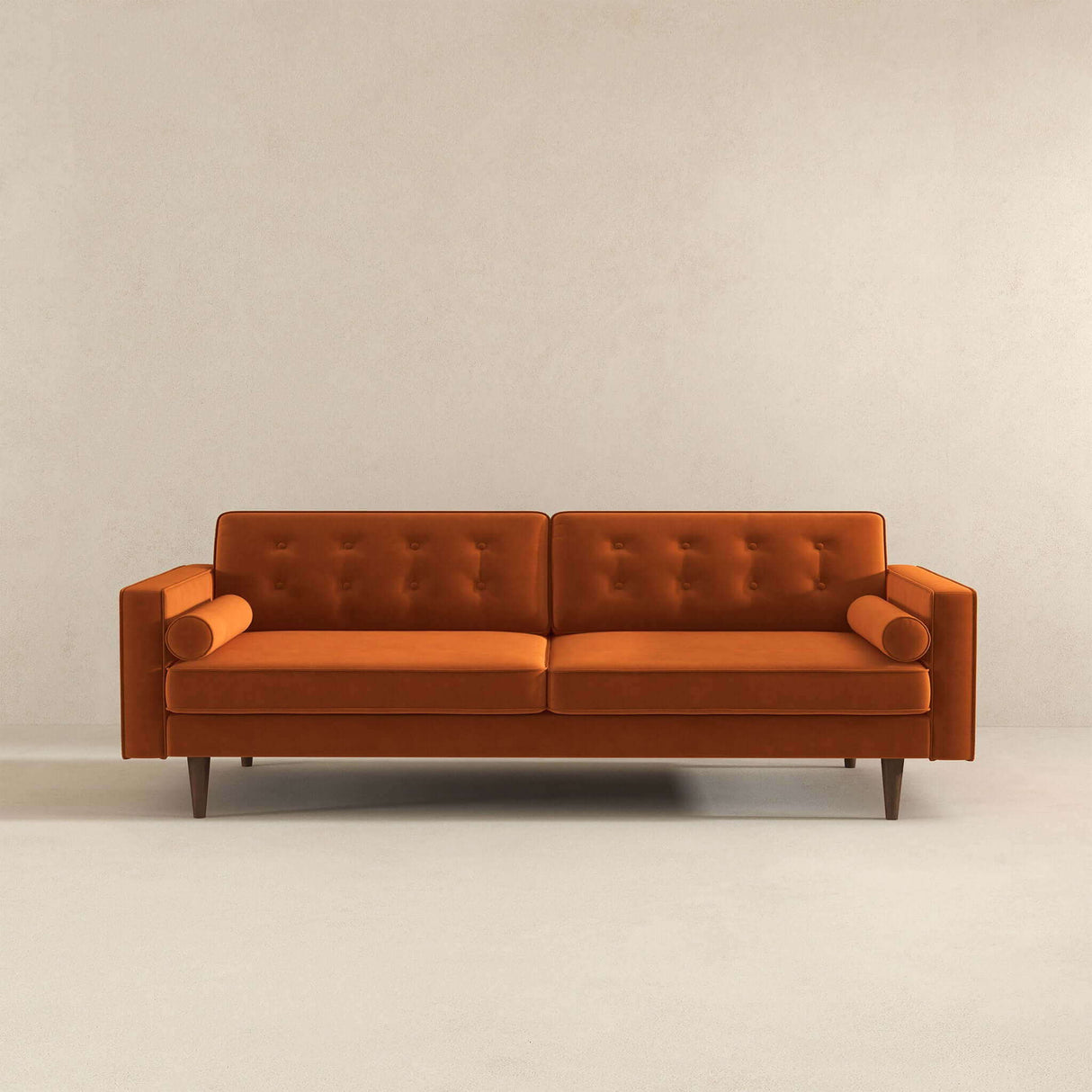 The Casey Mid-Century Modern Sofa features a sleek, minimalist design with wooden legs, an orange hue, tufted back cushions, and cylindrical bolster pillows on each armrest. It's set against a plain light beige wall and floor for a stylish look.