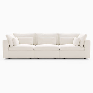 The Harmony Modular 3 Piece Sofa is a white, contemporary sectional displayed on a white background. It features four spacious seat cushions, a straight back, and several accent pillows, offering a clean and minimalist appearance.