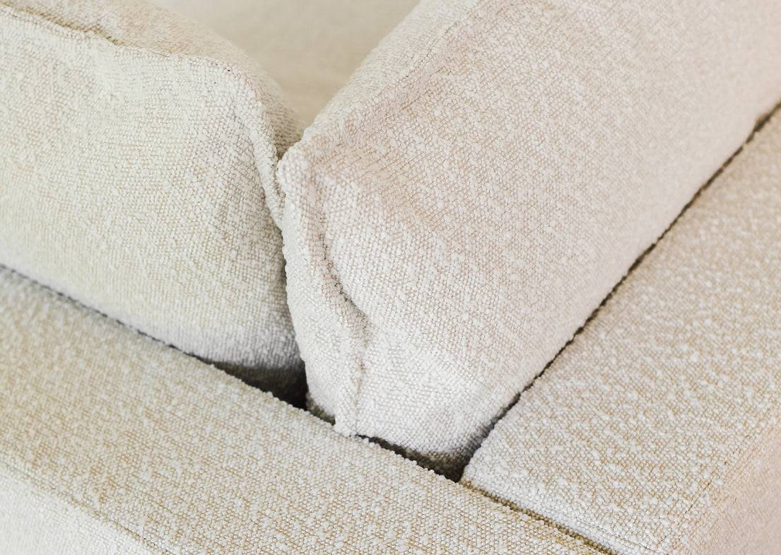 Close-up of the Kova L Shape with Ottoman, a beige textured fabric sofa featuring two cushions arranged at right angles to each other, showcasing the soft and plush material.