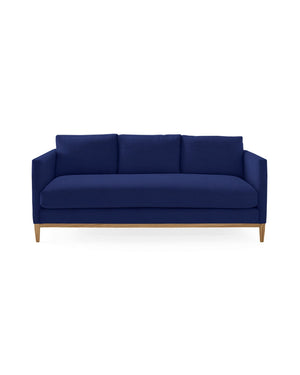 The Barton Sofa features a modern design with deep blue upholstery, clean lines, and wooden legs. It is a three-seater with a minimalistic style, complemented by three plush cushions on the backrest and set against a plain white background.