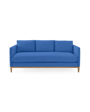 The Barton Sofa, a contemporary piece in blue, features three cushions and wooden legs, set against a simple white background.