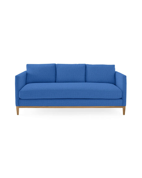 The Barton Sofa, a contemporary piece in blue, features three cushions and wooden legs, set against a simple white background.