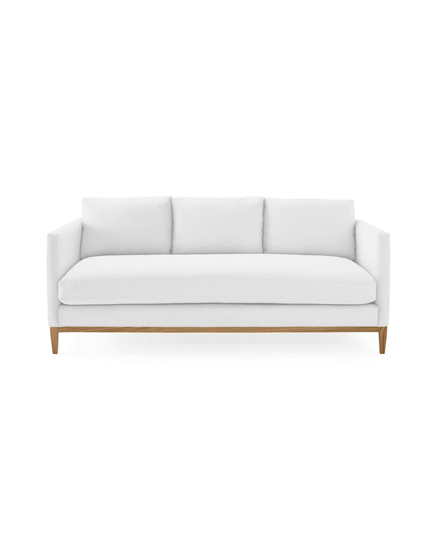 The Barton Sofa is a modern white piece featuring three cushions set against a clean, white background. It boasts a minimalist design with wooden legs, offering a stylish and contemporary look.