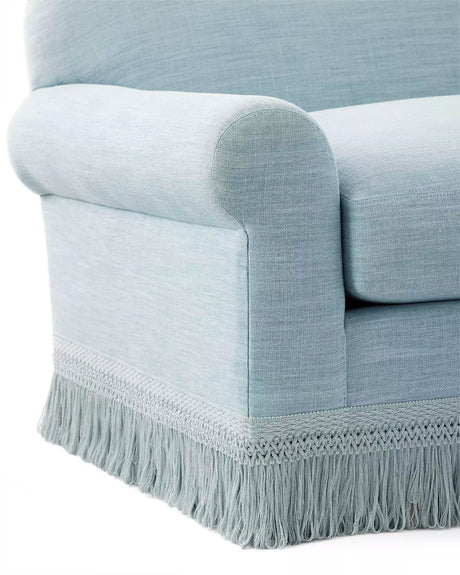 Close-up of the Cambridge Sofa in washed linen, featuring a light blue upholstery with rolled armrests and decorative fringe at the bottom. The fabric exhibits a soft, textured appearance, enhancing the sofa's elegant and classic look.