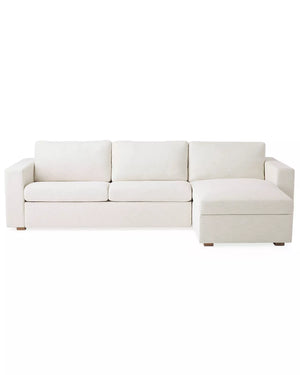 The Conover Sleeper Chaise Sectional is a light beige sofa featuring three cushions and a right-side chaise. It is designed with wide armrests and short wooden legs, showcased against a plain white background.