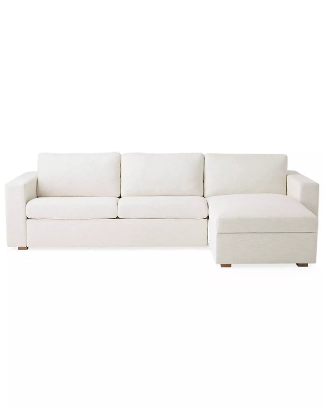 The Conover Sleeper Chaise Sectional is a light beige sofa featuring three cushions and a right-side chaise. It is designed with wide armrests and short wooden legs, showcased against a plain white background.