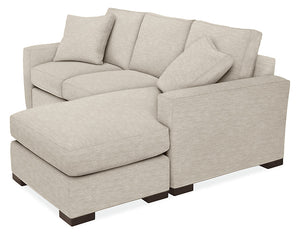 The Metro Sofas with Chaise is a light beige sectional featuring two seat cushions and a left-side chaise lounge. It comes with three back cushions and two matching throw pillows, all supported by dark wood legs and boasting a subtle woven fabric texture.