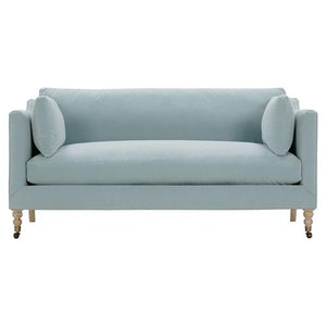 Introducing the Madeline French Grey Sofa: a spacious upholstered piece featuring two matching round pillows. This sofa showcases a modern design with elegant brown wooden legs ending in brass casters, creating a stylish and functional addition to any living room.
