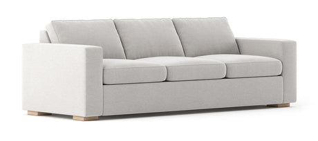 The Rio Sofa is a modern piece featuring a light gray finish, three cushions, and wide armrests. It boasts a minimalist design with short wooden legs, giving it a clean and sophisticated look.