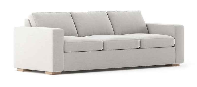 The Rio Sofa is a modern piece featuring a light gray finish, three cushions, and wide armrests. It boasts a minimalist design with short wooden legs, giving it a clean and sophisticated look.