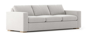 The Rio Sofa is a modern piece featuring a light gray finish, three cushions, and wide armrests. It boasts a minimalist design with short wooden legs, giving it a clean and sophisticated look.