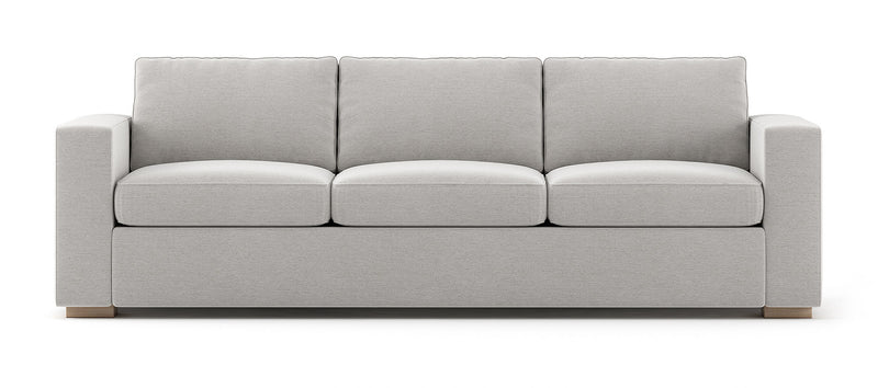 The Rio Sofa is a light gray three-seater with plush cushions and wide armrests, set against a white background with simple, modern design elements.