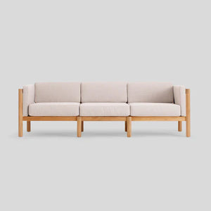 The Haven Sofa is a contemporary three-seater featuring light beige cushions and a wooden frame, displayed against a plain gray background.