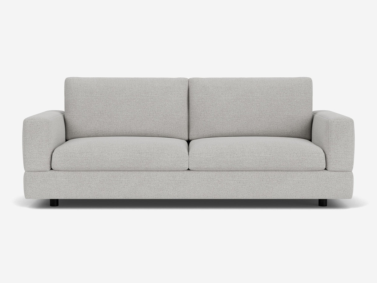 The Stage Track Sofa is a modern two-seater in light gray, featuring plush cushions and a minimalist design. It boasts square arms and a low-profile base, set against a plain white background.
